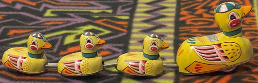 Four yellow tin litho wind-up ducks with painted red bills, orange feet, and colorful wing details arranged on a striped back
