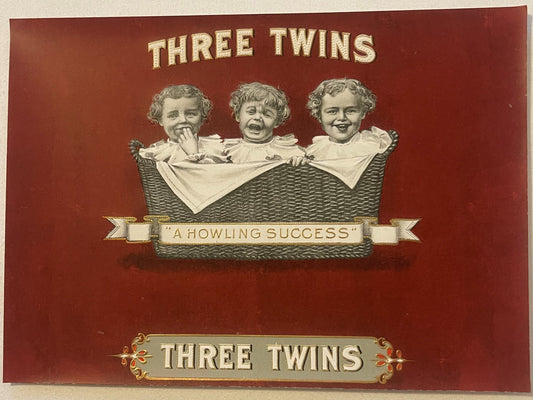 Vintage cigar box label with three babies in a wicker basket on burgundy background, gold embossed text reading "Three Twins"
