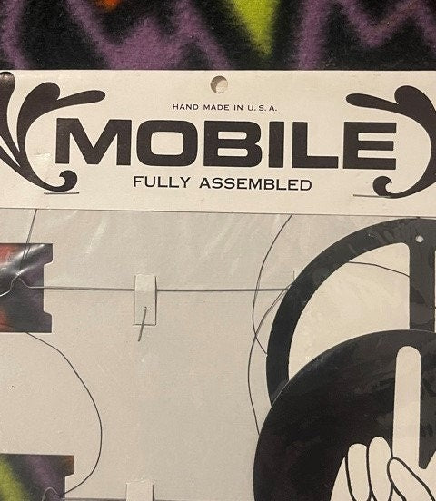 Close-up of vintage mobile packaging label reading "MOBILE FULLY ASSEMBLED HAND MADE IN U.S.A." with decorative flourishes an