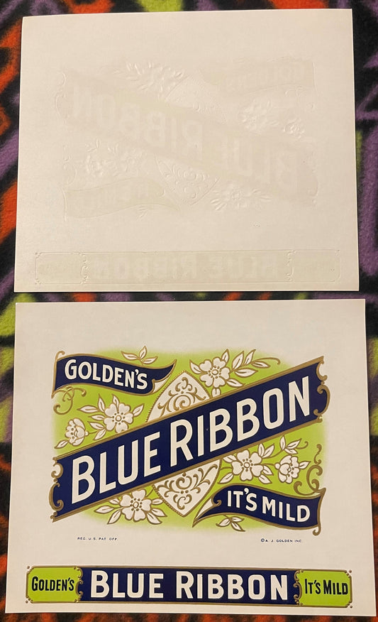 Two vintage cigar labels displayed on colorful patterned fabric; top label embossed in cream with decorative flourishes, bott