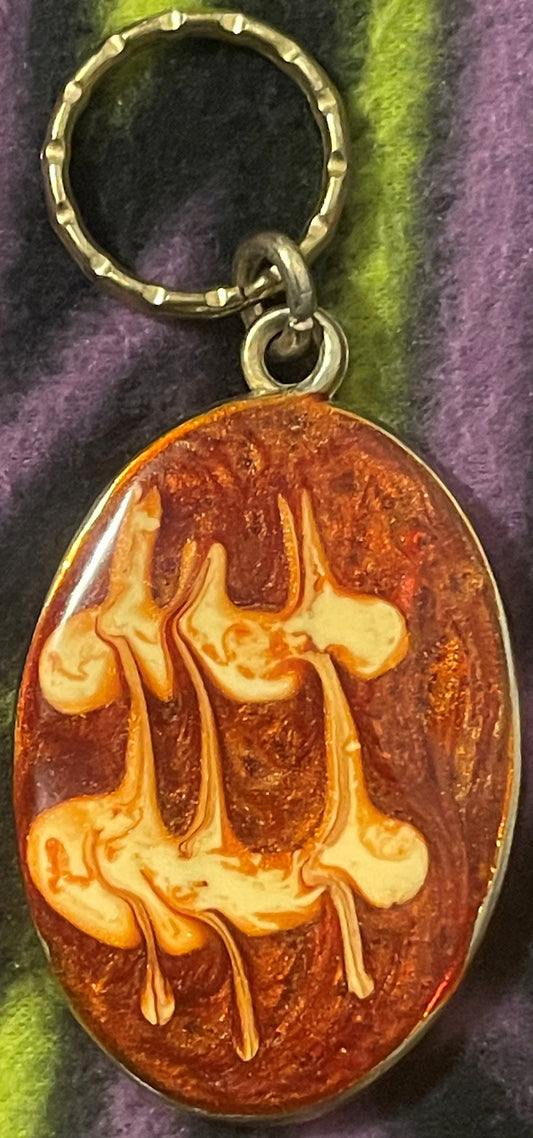 Oval amber and cream resin pendant keychain with swirled pattern, hanging from textured metal ring against striped fabric bac