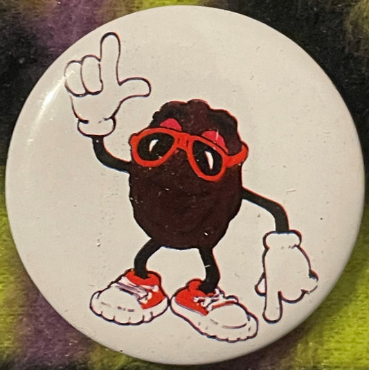 Circular pinback button featuring a dark brown cartoon character wearing red-framed glasses and red sneakers, with one hand r