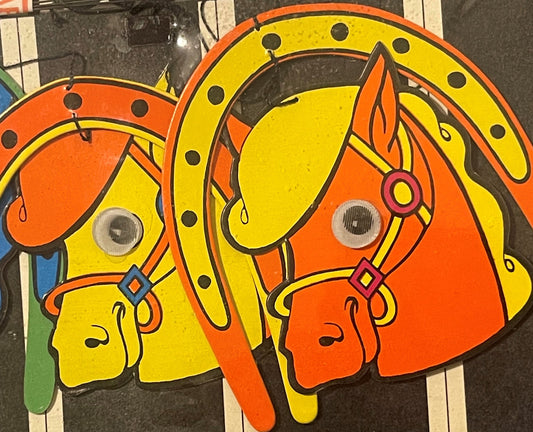 Two colorful carousel horses with yellow and orange painted bodies, googly eyes, and decorative saddles displayed against a d