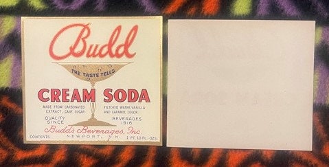 Vintage Budd cream soda label with red script text on cream background, displayed next to blank label reverse, on patterned f