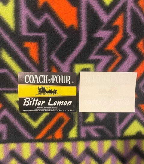 Vintage Coach and Four Bitter Lemon soda label with stagecoach silhouette, displayed on colorful geometric patterned fabric b