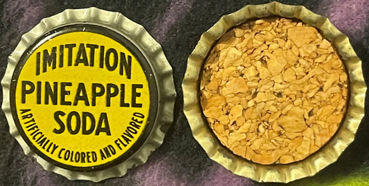 Two views of a yellow and black cork bottle cap labeled "Imitation Pineapple Soda – Artificially Colored and Flavored," showi