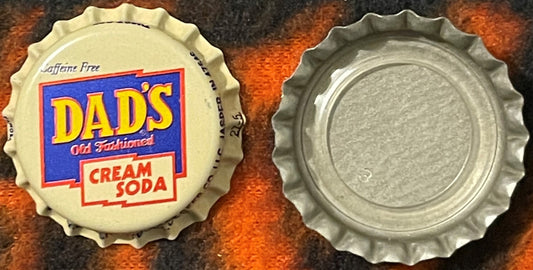 Vintage Dad's Old Fashioned Cream Soda bottle cap showing front and back views on rust-colored surface, caffeine-free label v