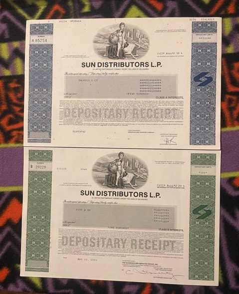 Two vintage Sun Distributors L.P. stock certificates with blue and green decorative borders, displayed flat on colorful patte