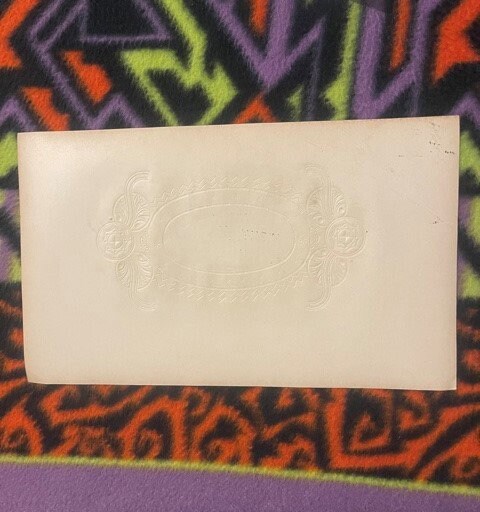 Cream-colored embossed cigar label with ornate decorative design on colorful patterned fabric background