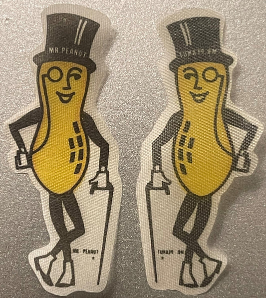 Two vintage Mr. Peanut cloth stickers with yellow peanut bodies, black top hats, monocles, and formal wear, shown front and b
