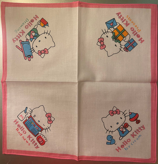 Unfolded Hello Kitty cotton napkin showing four panels with character illustrations and colored text on cream fabric with pin