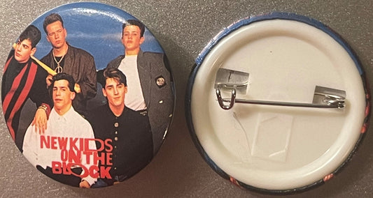 Vintage NKOTB pinback button showing five band members in dark clothing against blue background, with back side displaying pi
