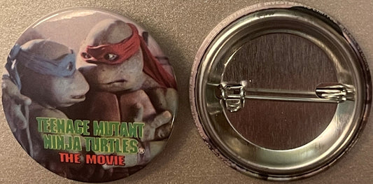 Front and back of circular pin featuring two Teenage Mutant Ninja Turtles characters in gray and red masks with "TEENAGE MUTA