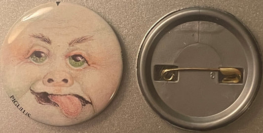 Front and back of a round pinback button featuring a grotesque baby face with green eyes, protruding tongue, and "PIGULUS" te