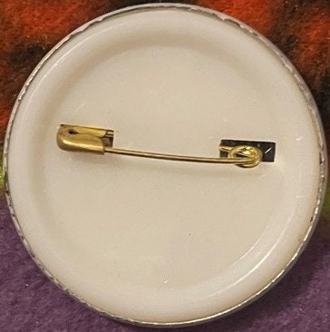 Vintage tennis-themed California Raisin pin with gold-tone backing displayed on white circular card against colorful fabric b