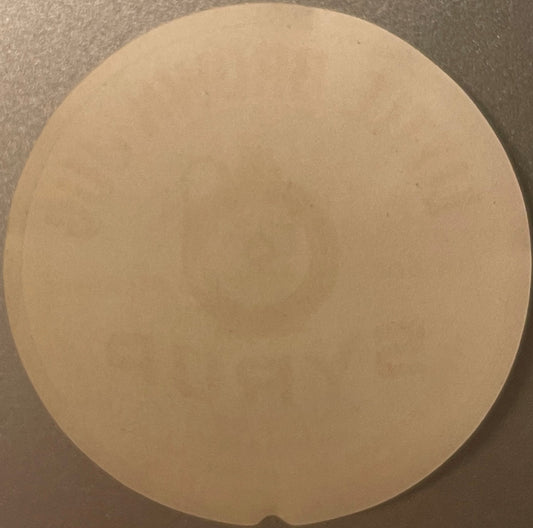 Blank cream-colored circular label on gray surface, viewed from above