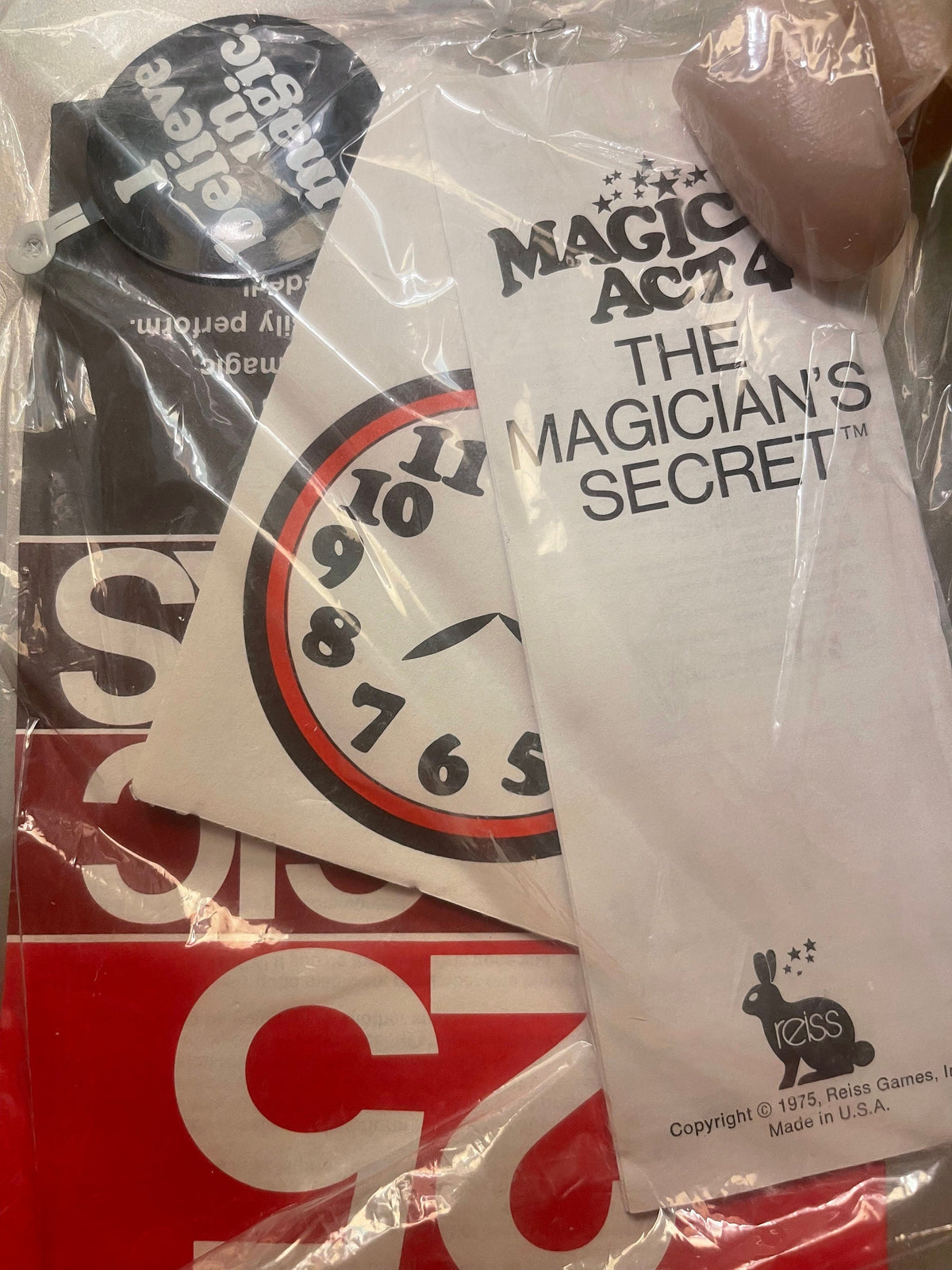 Vintage magic trick kit in plastic packaging showing instruction manual and brown prop item, copyright 1975 Reiss Games