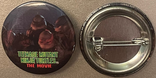 Front and back of a circular metal pin featuring Teenage Mutant Ninja Turtles characters in dark tones with green and red tex