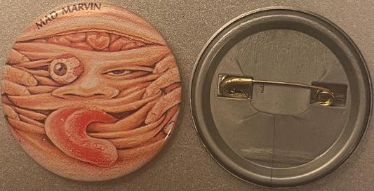 Front and back of a terracotta pinback button featuring embossed grotesque face with bulging eyes and text reading "MAD MARVI