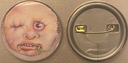 Front and back of a vintage pin badge featuring a grotesque face with closed eyes and protruding teeth dripping green slime,