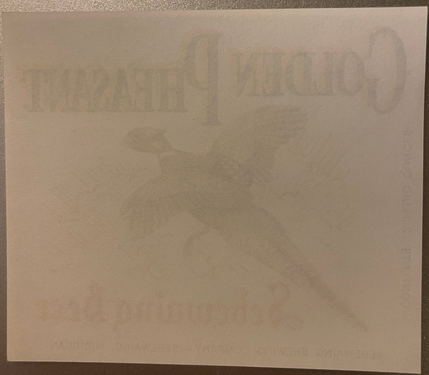 Faded vintage beer label with embossed Golden Pheasant branding and Michigan brewery text, displayed on cream paper against d