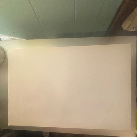 Blank cream-colored vintage movie poster displayed flat on a dark surface against a light ceiling