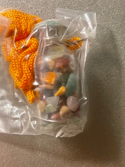 Vintage glass vial necklace with colorful gemstone chips in orange, yellow, green, and red tones, displayed in clear plastic