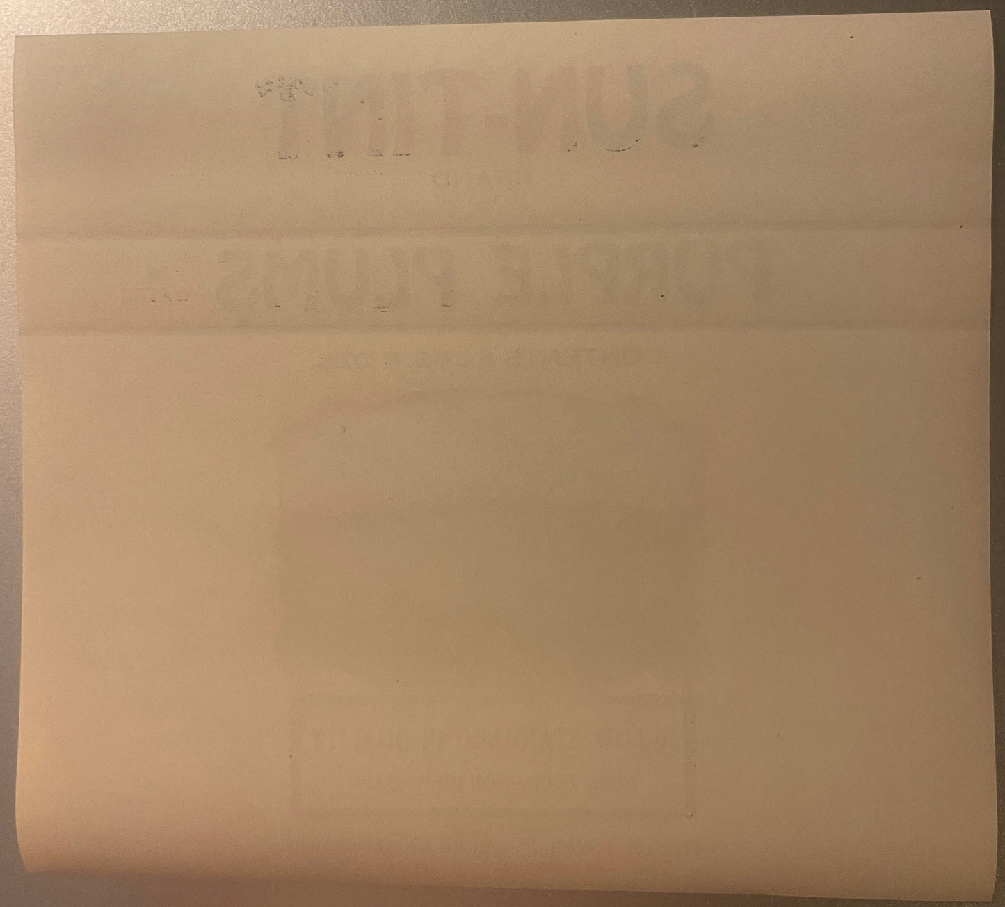 Aged peach-colored fruit crate label with faded text, folded creases visible, photographed flat against neutral background