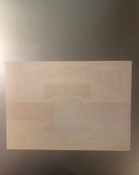 Faded vintage pear crate label on cream background with partially visible text and imagery, photographed flat against a wall