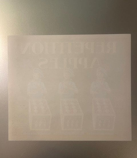 Faded cream-colored vintage apple crate label with embossed text and repeated imagery, photographed flat against gray backgro