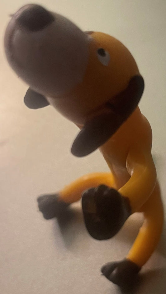 Vintage bendable dog toy figure with tan body and dark gray head, held upright showing articulated limbs and poseable design