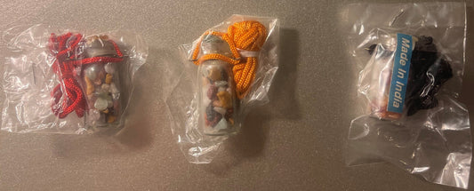 Three sealed plastic bags containing glass vials with colorful fabric wraps (red, orange, black) and gemstone chips inside, o