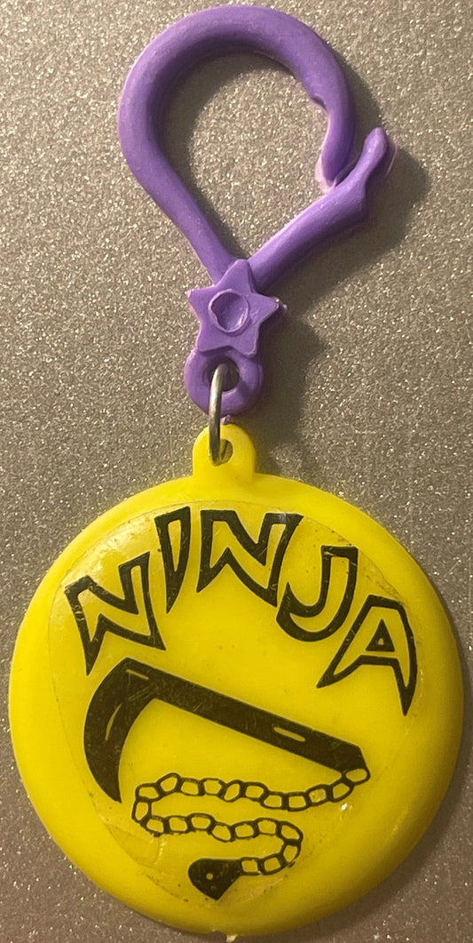 Purple clip keychain with star detail attached to yellow round charm printed with "NINJA" text and black ninja weapon imagery