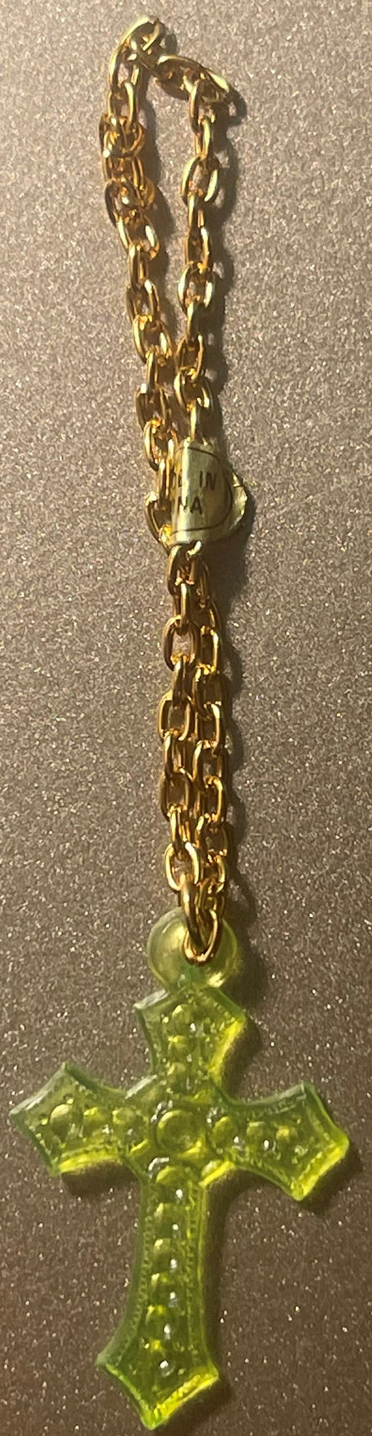 Gold-tone chain bracelet with translucent yellow-green cross pendant featuring decorative dot patterns, displayed on textured