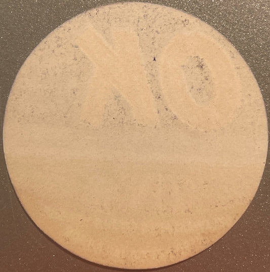 Circular tan citrus crate label with small dark specks, photographed flat against dark background, showing weathered surface