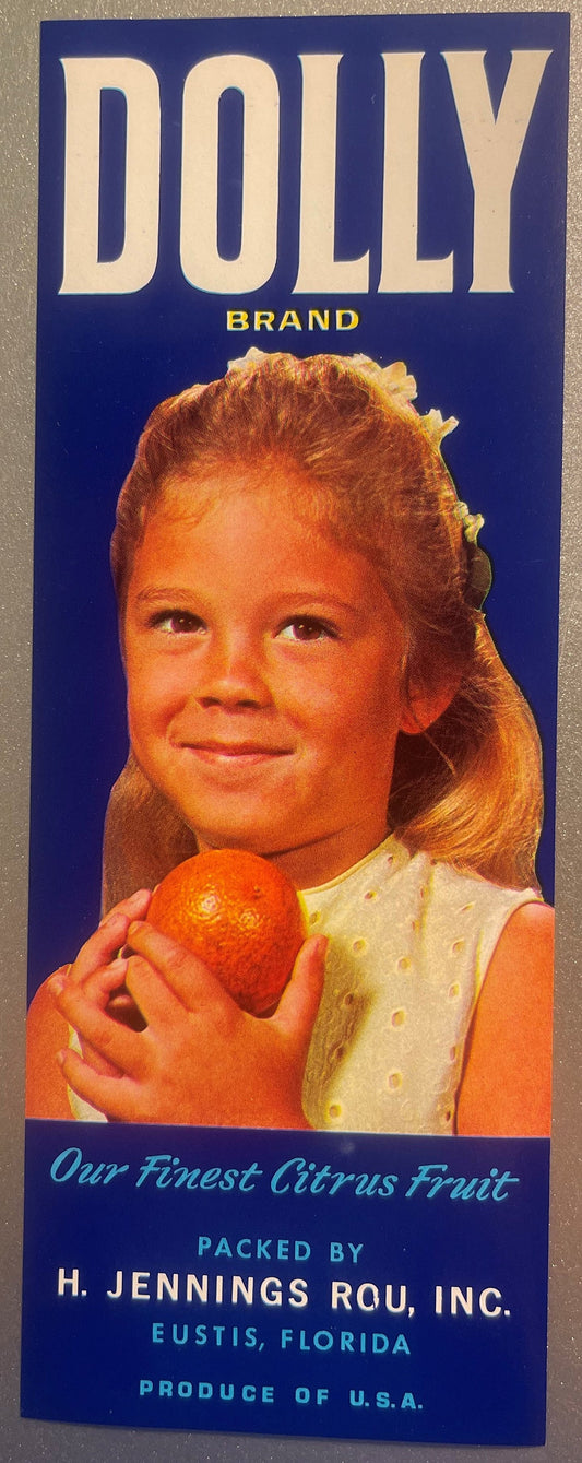 Vintage Dolly Brand citrus crate label featuring a smiling girl holding an orange against a navy blue background, with text i