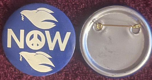 Front and back of blue pinback button with cream dove and "NOW" text with peace symbol, shown against burgundy fabric