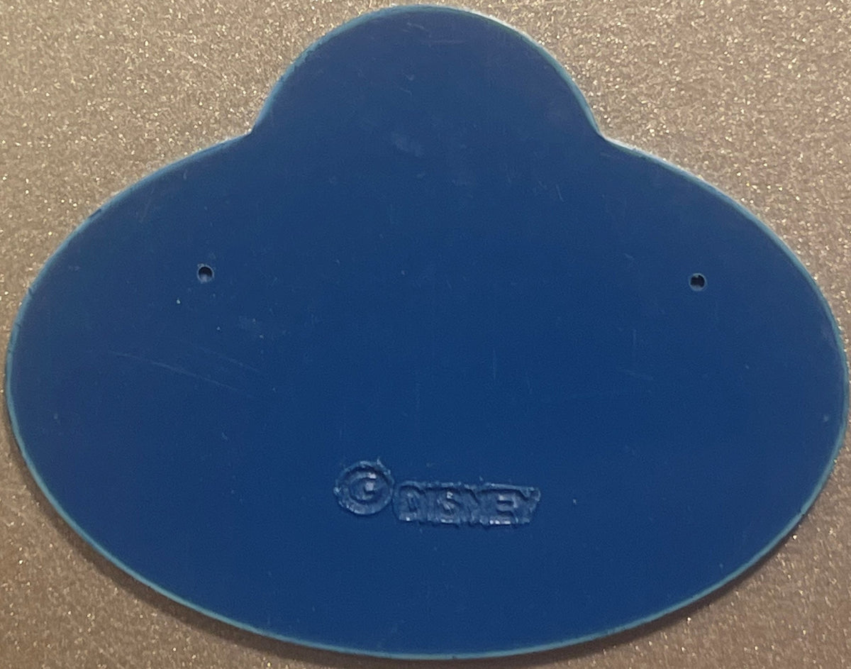 Blue Disney cast member badge with embossed logo, two mounting holes visible, photographed flat on textured surface