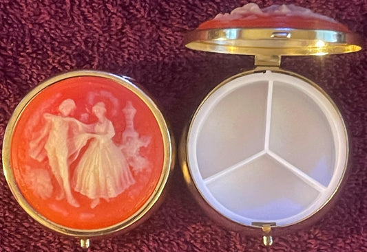 Two open compact cases with brass trim on burgundy fabric: left shows coral cameo with carved dancing couple; right displays