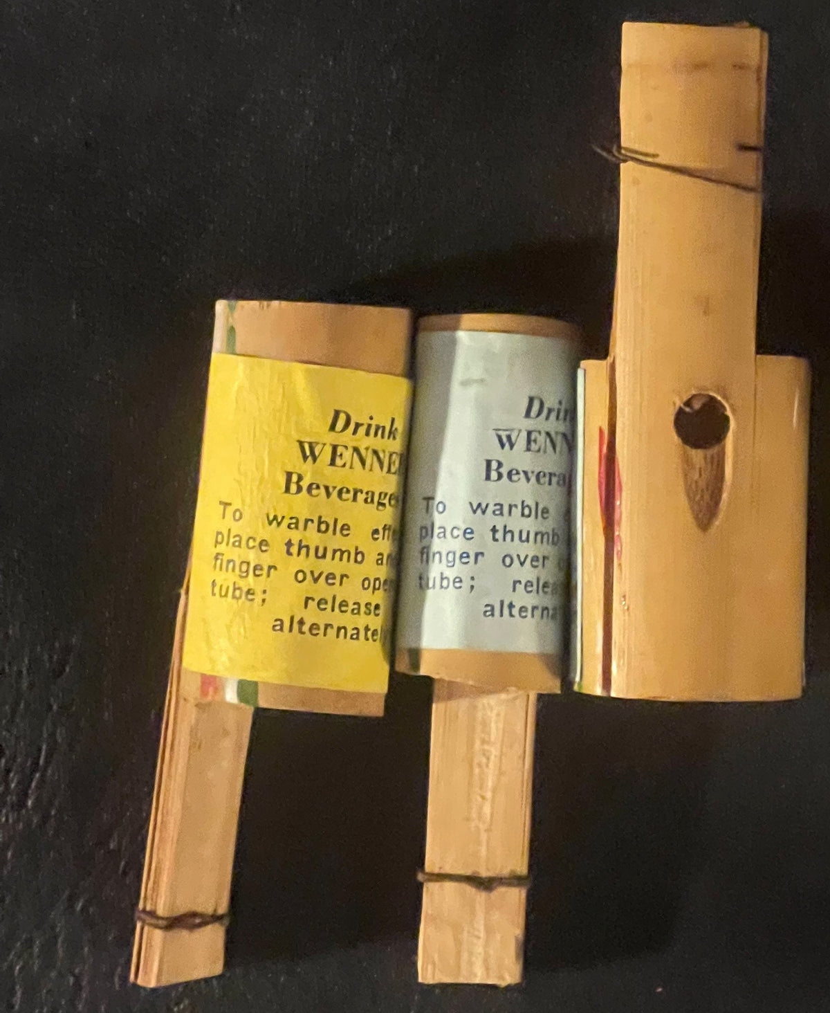 Wooden warbler toy with two cylindrical beverage bottles labeled "Drink Wenner Beverage" in yellow and white, shown against b