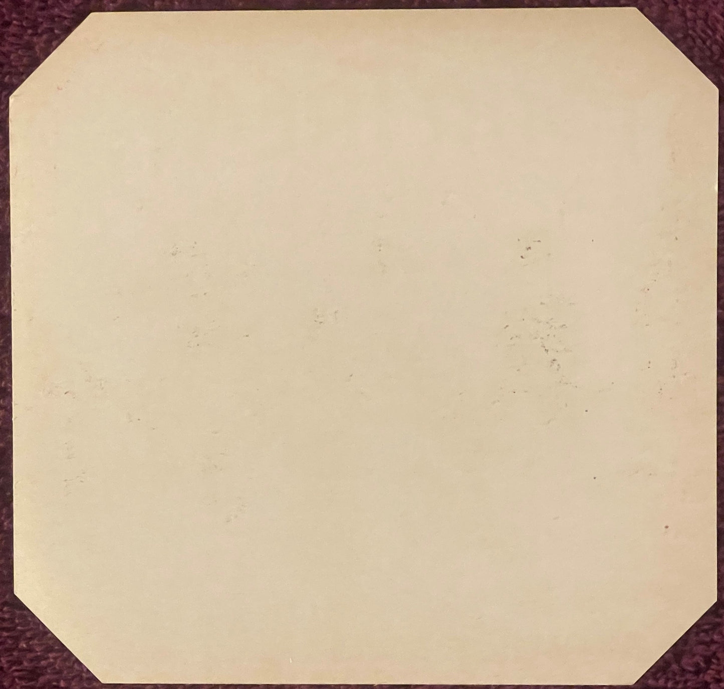 Blank cream-colored vintage cigar label with rounded corners on burgundy fabric background, showing age spots and patina