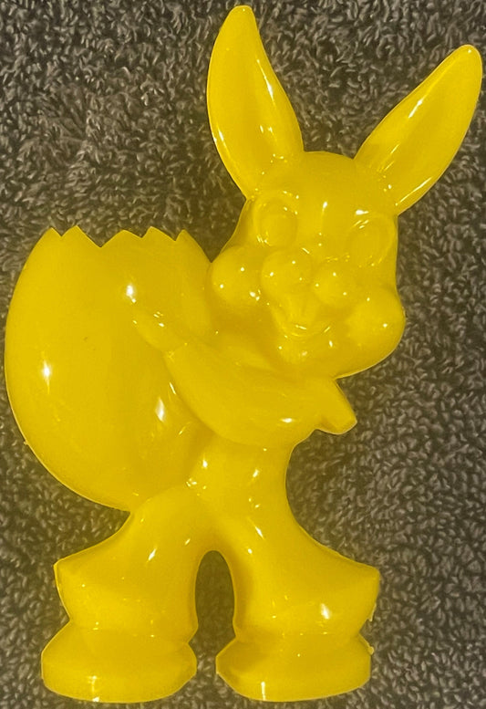 Bright yellow hard plastic bunny rabbit figurine with long ears and textured body against gray fabric background