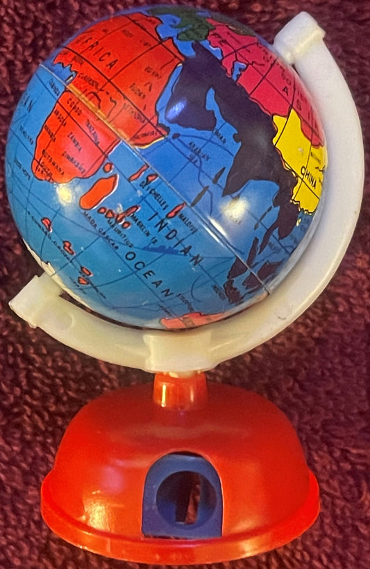 Colorful globe pencil sharpener with red base mounted on burgundy fabric background, showing North America and Asia in red, b