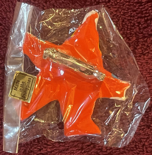 Bright red plastic clown star pin with gold accents in clear cellophane package against burgundy fabric, "Made in the Philipp