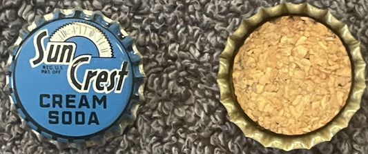 Two vintage Sun Crest cream soda bottle caps shown front and back against textured gray fabric, displaying blue label with su