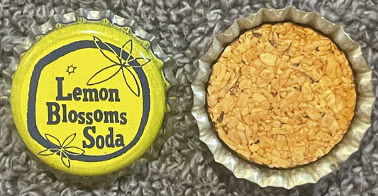 Vintage yellow and black Lemon Blossoms Soda bottle cap shown open and closed, displaying cork interior, on textured gray