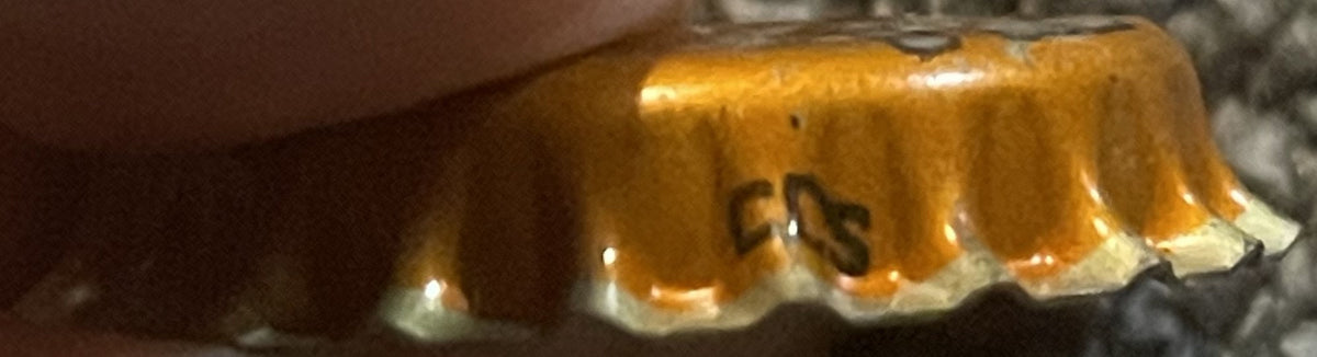 Antique Hires Root Beer cork bottle cap viewed from above, showing golden-orange metallic surface with embossed "HIRES" text and white cork lining visible around the edges.