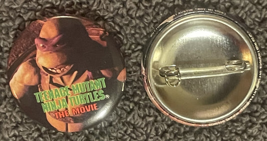 Front and back of a circular pin badge featuring a Teenage Mutant Ninja Turtles character in red mask with "THE MOVIE" text i