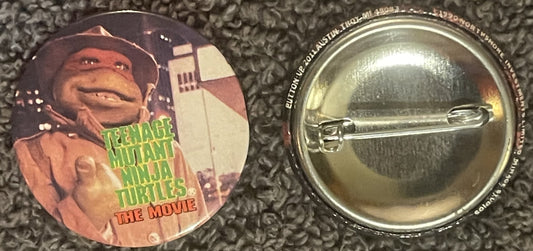 Vintage TMNT movie pin showing character giving thumbs up with green text, displayed front and back on textured fabric backgr