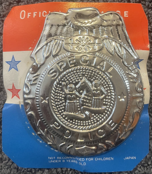 Vintage silver-tone metal police badge with eagle and shield design on red, white and blue cardstock backing, made in Japan.